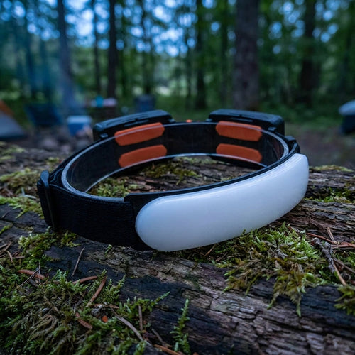 Rechargeable LED headlamp 1500 lumens resting on a mossy log at a forest campsite