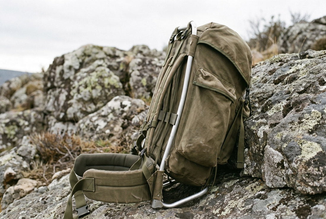 An empty backpack standing upright on bare rock, hip belt and frame visible from the side