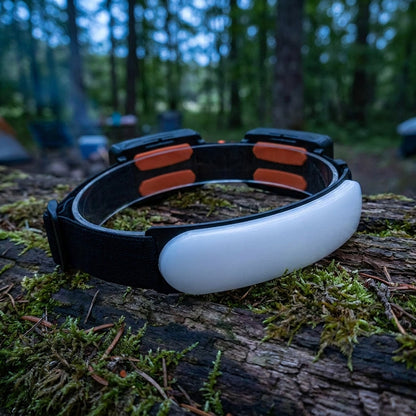 Rechargeable LED headlamp 1500 lumens resting on a mossy log at a forest campsite